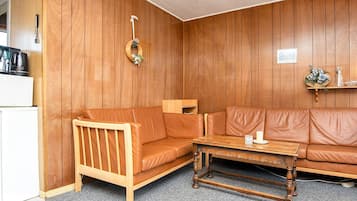 Uma sala de estar acolhedora com parede de madeira, um sofá de couro marrom, uma mesa de centro de madeira e um pequeno armário de madeira.