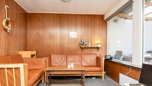 Una habitación con pared de paneles de madera, un sofá de cuero marrón, una mesa de centro de madera, un escritorio pequeño con una computadora y una ventana con vistas al exterior.