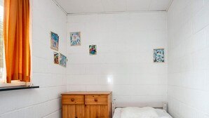 A small, single-bed room with white walls, a wooden wardrobe, and a window with orange curtains. - 3 Person Holiday Home in Sydals (Sydals)