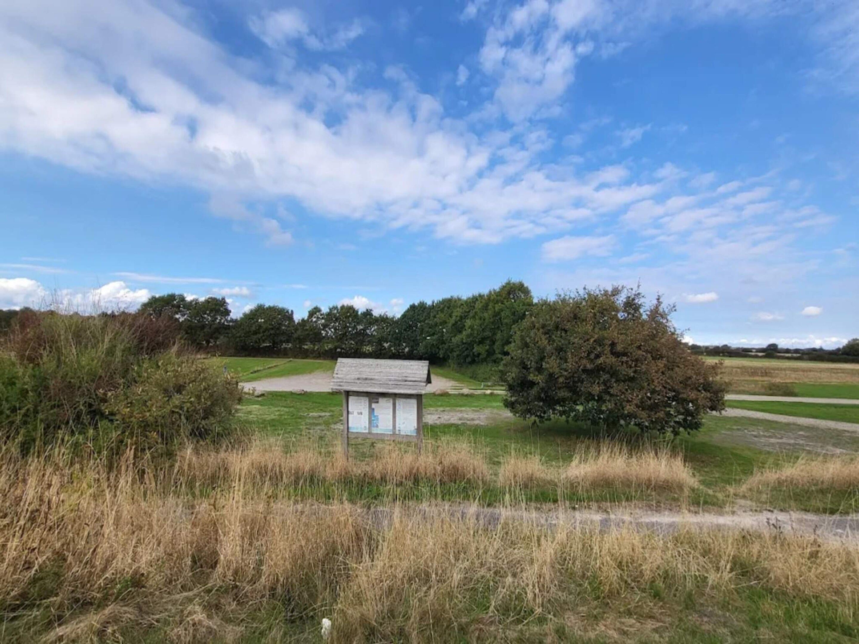 Ein kleines Holzgebäude in einem grasbewachsen Feld unter blauem Himmel.
