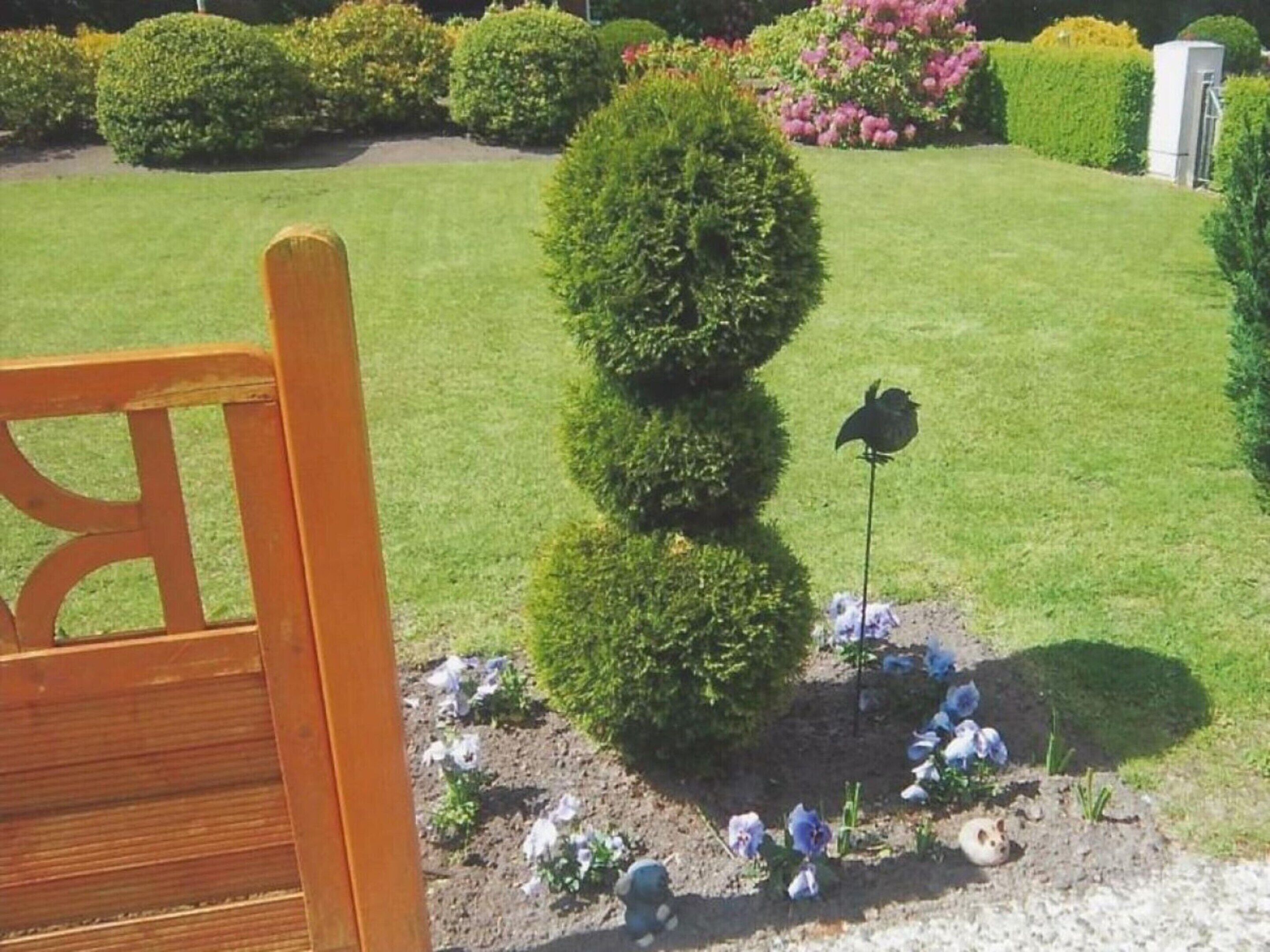 A well-maintained garden with neatly trimmed hedges, a bird feeder, and a variety of flowers.