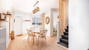 A modern kitchen with white cabinets, a wooden dining table, and a staircase leading to another level. - Garden Villa Steps From Beaches (Koksijde)