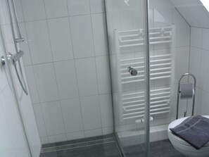 A modern bathroom with a glass shower enclosure, a white tiled floor, and a glass door leading to the shower. - "norderney" in the Achter de Waterkant House (Büsum)