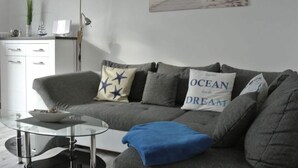 A modern living room with a grey sofa, a glass coffee table, and a painting of a beach scene. - "norderney" in the Achter de Waterkant House (Büsum)