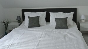 A neatly made bed with white bedding and two gray pillows, a black headboard, and two bedside tables with lamps. - "norderney" in the Achter de Waterkant House (Büsum)