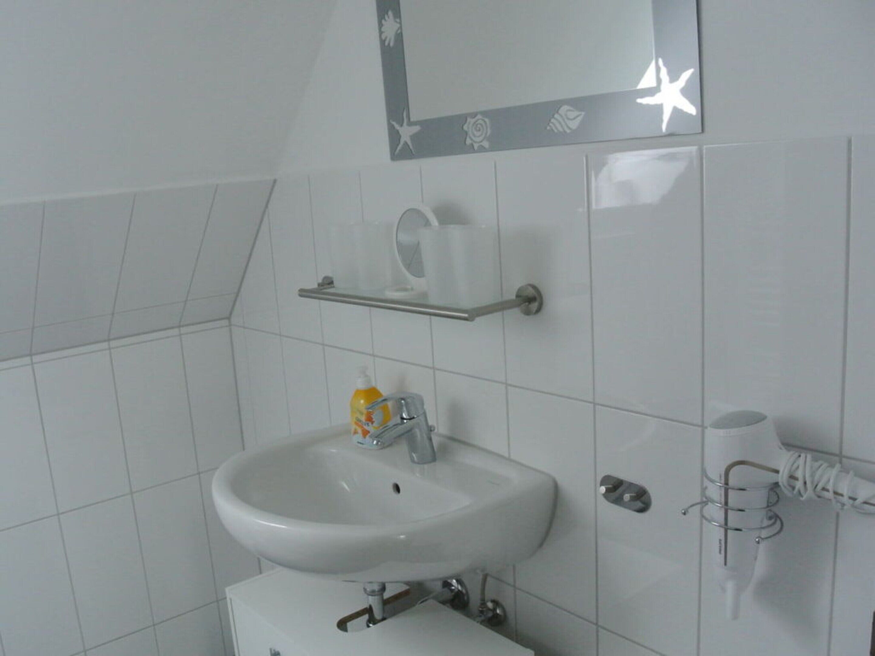 Un baño con lavamanos blanco, un espejo con diseño de estrella y un dispensador de jabón en una repisa.