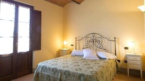 A bedroom with a bed, two bedside tables, a window with curtains, and a brick ceiling. - Apartment in Bolgheri Near Tuscan Beaches (Castagneto Carducci)