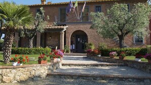 A traditional brick building with a central arched entrance, surrounded by a gravel pathway and potted plants. - Apartment in Bolgheri Near Tuscan Beaches (Castagneto Carducci)
