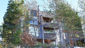 A multi-level cabin with a wooden exterior, surrounded by trees and rocky terrain. - 8 Person Holiday Home in Sondeled (Risør)