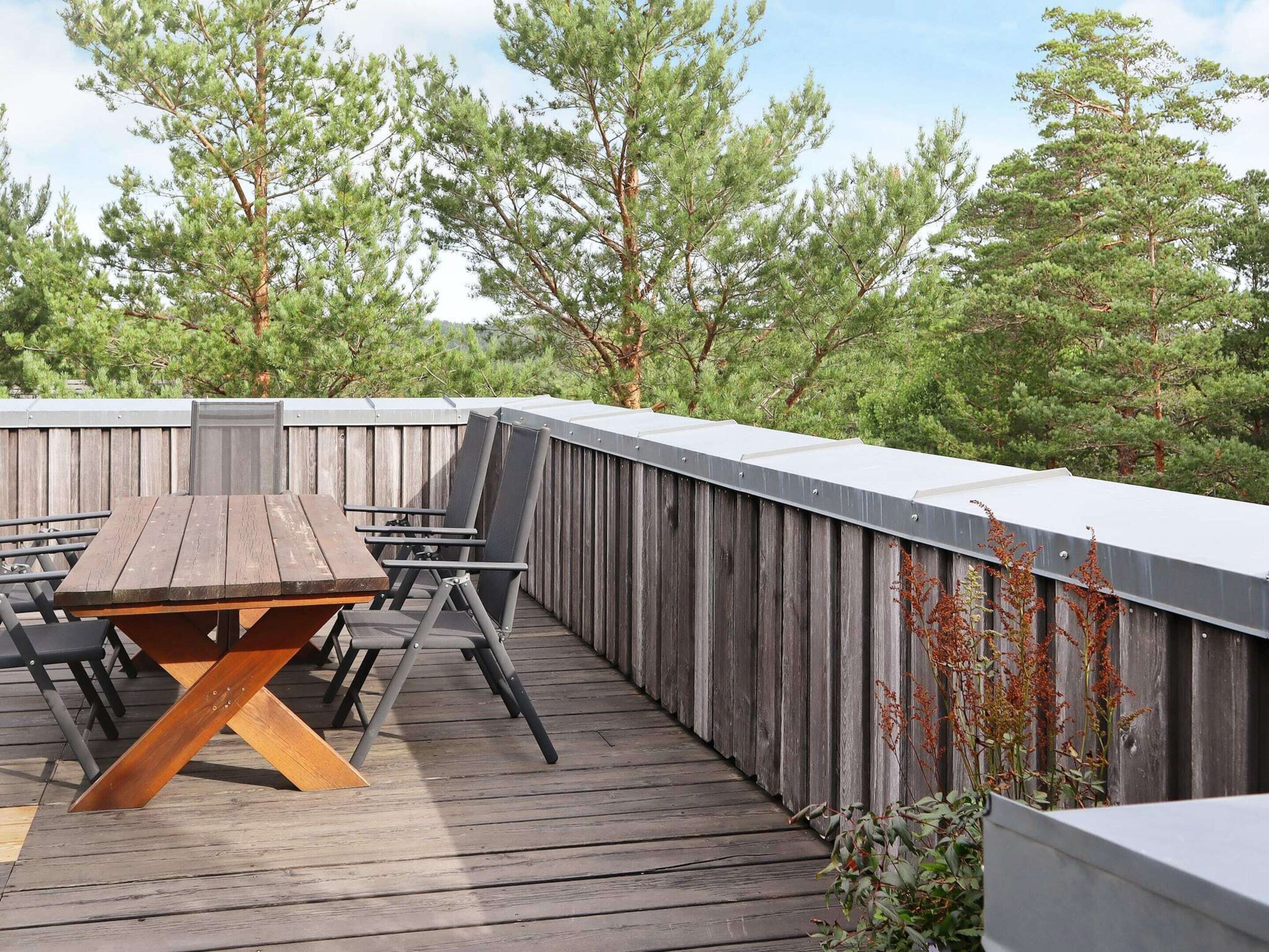An outdoor deck with a wooden table and chairs, surrounded by a wooden fence and trees.