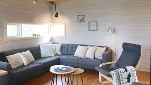 A modern living room with a grey sectional sofa, a round coffee table, a blue armchair, and a wooden ceiling. - 8 Person Holiday Home in Sondeled (Risør)