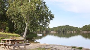 A lakeside picnic area with a wooden table and benches, surrounded by trees and a calm lake. - 8 Person Holiday Home in Sondeled (Risør)