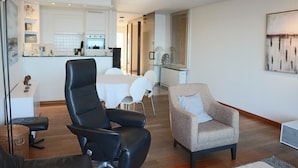 Una sala de estar moderna con un sillón de cuero negro, un sillón beige y un comedor con mesa y sillas blancas.