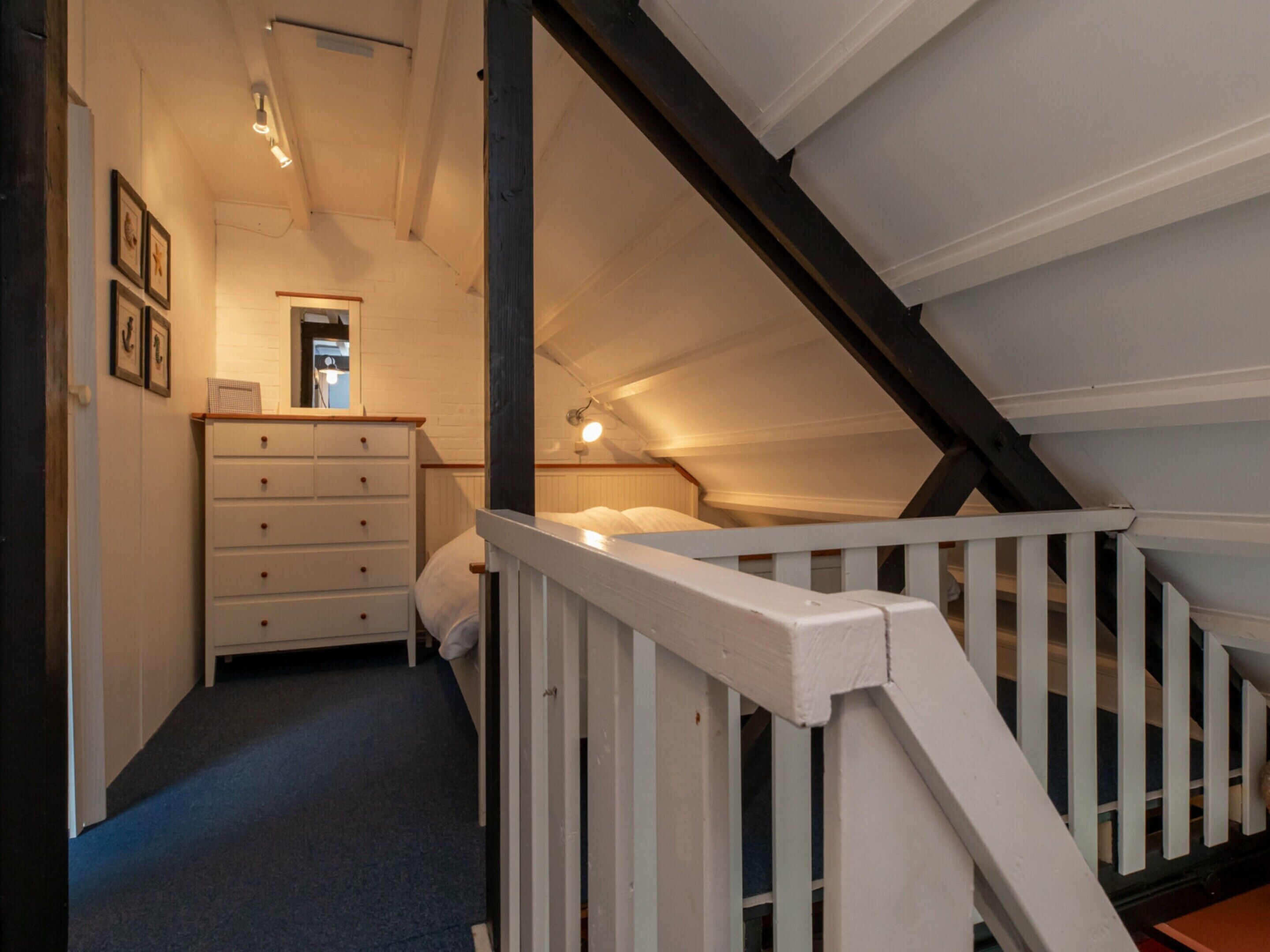 A narrow staircase leading to a loft bedroom with a white dresser and a bed.