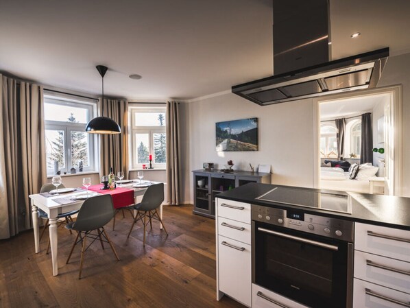 A modern kitchen with a dining area, wooden flooring, and a large window with curtains. - Holiday Apartment Waldfrieden (Altenberg)