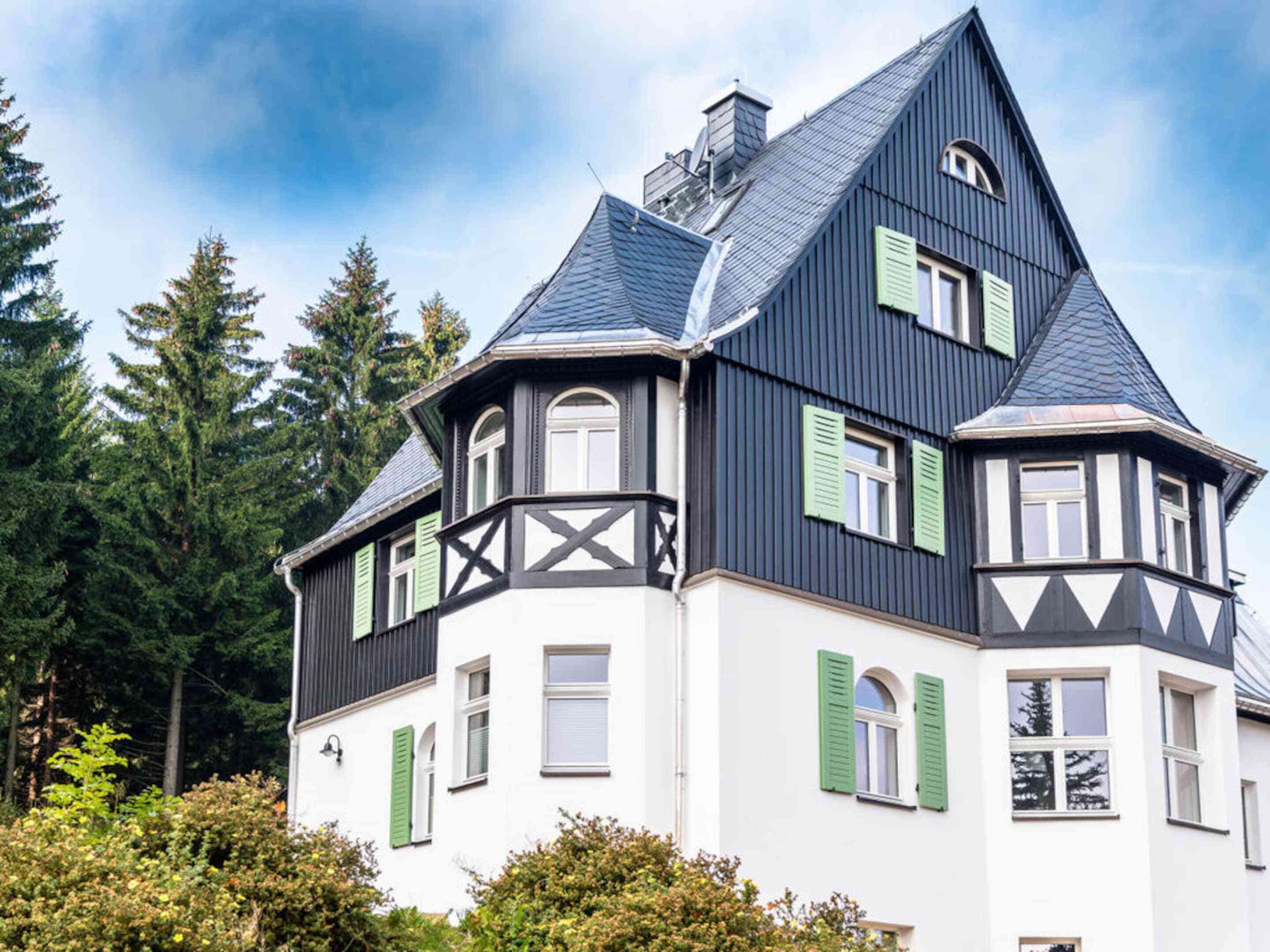 Ein großes, zweistöckiges Haus mit einem steilen Dach, weißen Wänden und grünen Fensterläden.