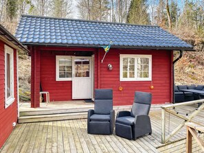 A red cabin with a tiled roof, a deck, and two wicker chairs.