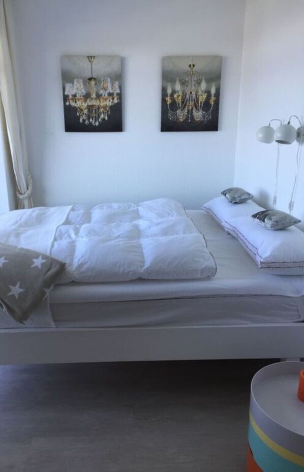 A bedroom with a bed, two wall-mounted paintings of chandeliers, a bedside lamp, and a bedside table. - Pearl With sea View Comfortable Vacation Home (Grossenbrode)