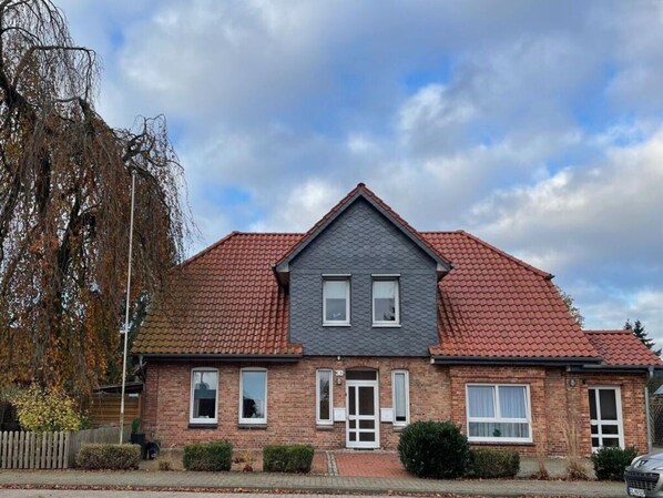 A two-story house with a red-tiled roof, brick walls, and a grey front facade.
