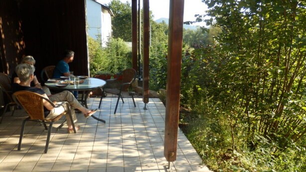 An outdoor patio with a round table and chairs, surrounded by greenery and a building in the background. - Holiday Apartment at the Linden Tree (Dernbach)
