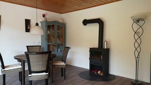 A dining area with a round table and four chairs, a blue cabinet with glass doors, a black wood-burning stove, and a floor lamp. - Holiday Apartment at the Linden Tree (Dernbach)