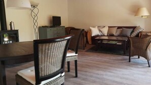 A cozy living room with a wooden ceiling, a dining table, chairs, a sofa, and two lamps. - Holiday Apartment at the Linden Tree (Dernbach)