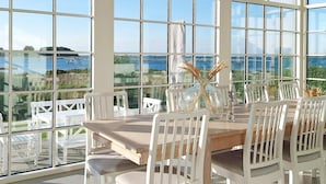 A dining area with a large table and white chairs, large windows offering a view of the sea and landscape. - 5 Star Holiday Home in Assens (Assens)
