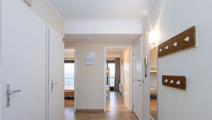 Ein Hotelgang mit Holzböden, weißen Wänden und Meerblick durch ein Fenster.