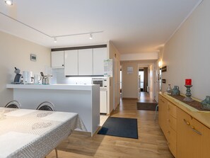 A modern kitchen with white cabinets, a dining table with a patterned tablecloth, and a wooden floor. - Charming Apartment Near the Beach (Middelkerke)