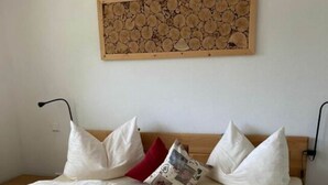 A neatly made bed with white linens and pillows, a wooden headboard, and a wall-mounted artwork above. - Lovely Apartment in Baden-wurttemberg (Oberkirch)
