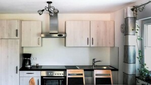A compact kitchen with light wood cabinets, a black countertop, and a stainless steel range hood. There is a dining table with chairs and a potted plant by the window. - Lovely Apartment in Baden-wurttemberg (Oberkirch)