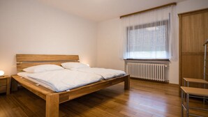 A bedroom with a wooden bed, a nightstand, a radiator, and a window with curtains. - Holiday Home Villa Bauer (Traben-Trarbach)