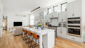 A modern kitchen with white cabinetry, a central island with bar stools, a large window, and a built-in oven.