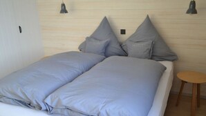 A bed with grey bedding, a small round wooden table, and two pendant lights. - 8 in het Huis Meerloft (Norderney)