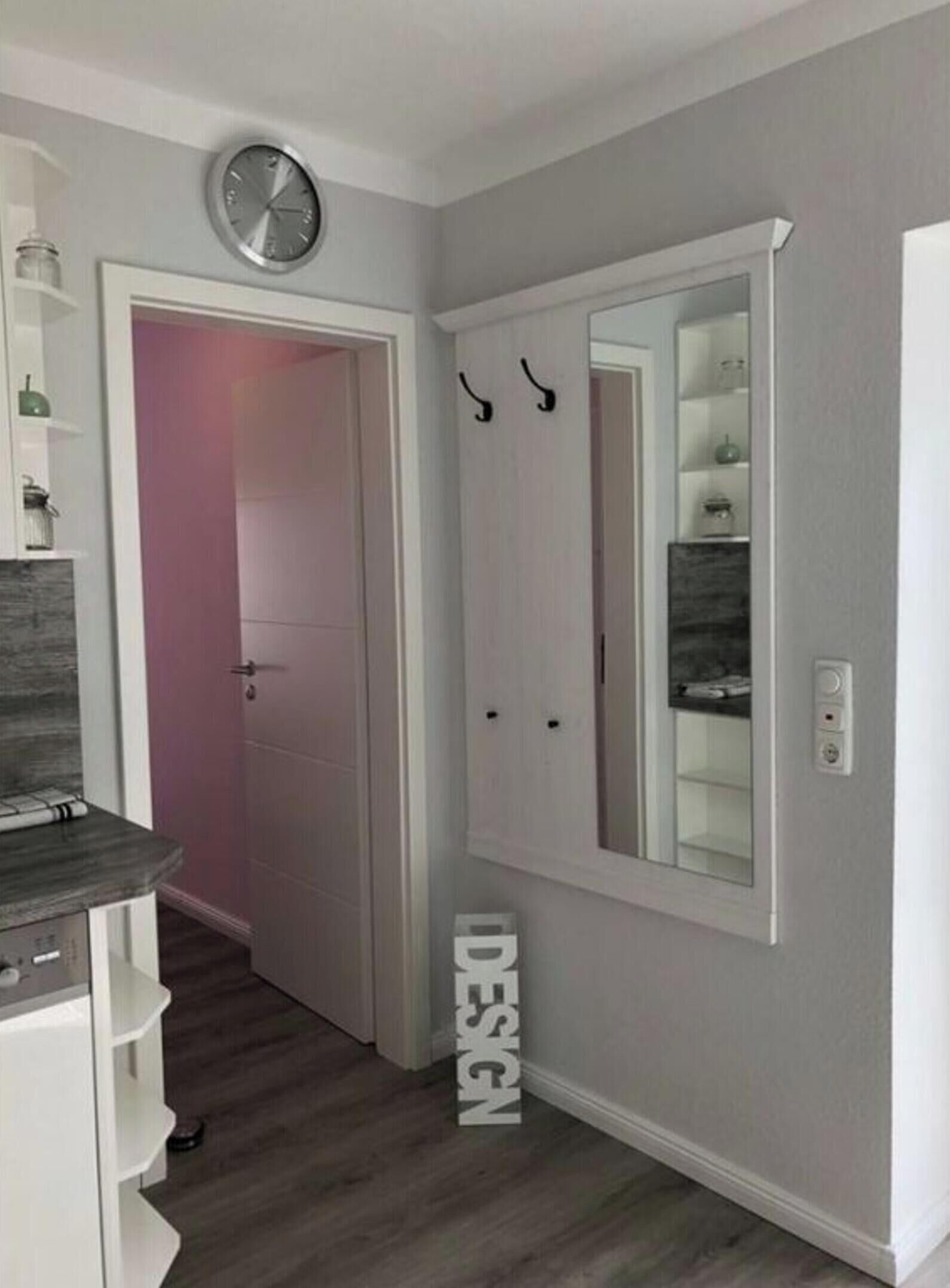A hallway with a white door, a clock, and a mirror on the wall.