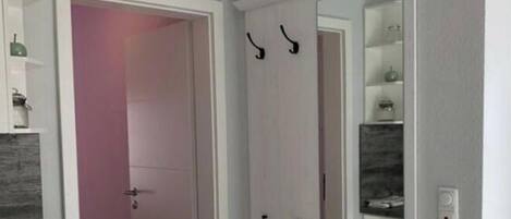 A hallway with a white door, a clock, and a mirror on the wall.