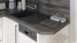 A modern kitchen with white cabinets, a dark backsplash, a built-in sink, and a coffee maker. - Romantic Apartment Near Seabeach (Büsum)
