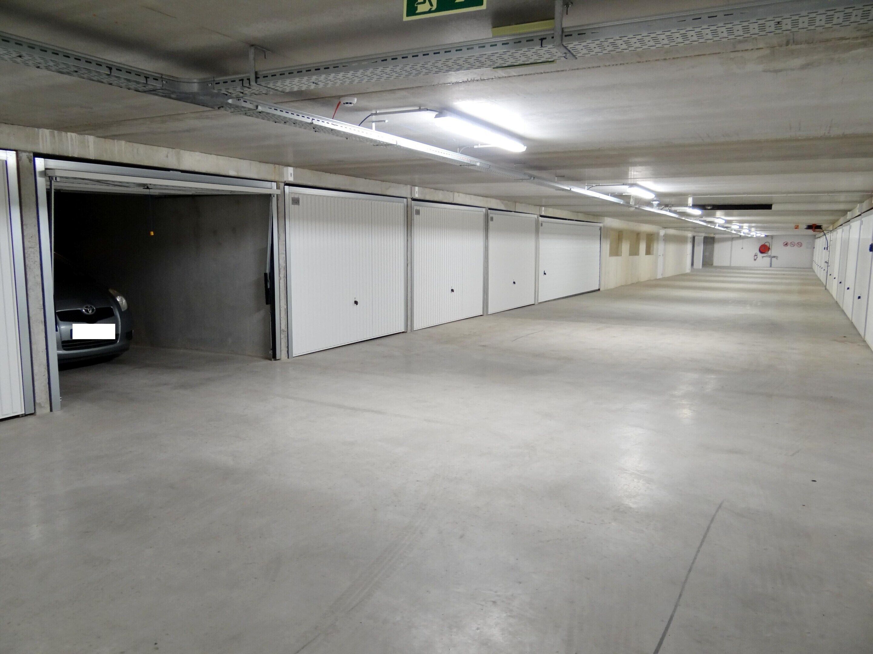 Un long parking souterrain, vide, avec des portes blanches et un sol gris.