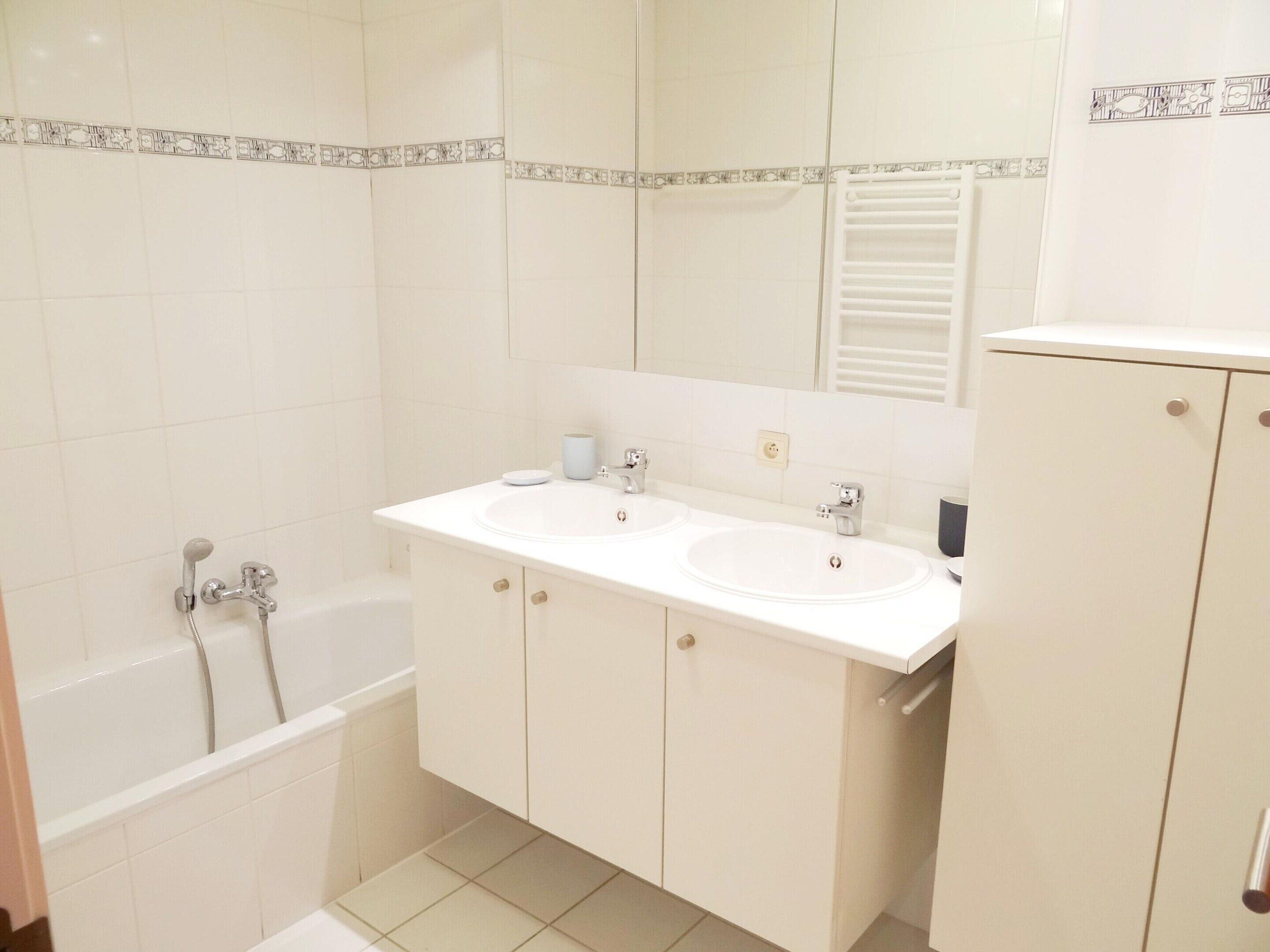 A bathroom with two sinks, a bathtub, and a cabinet.