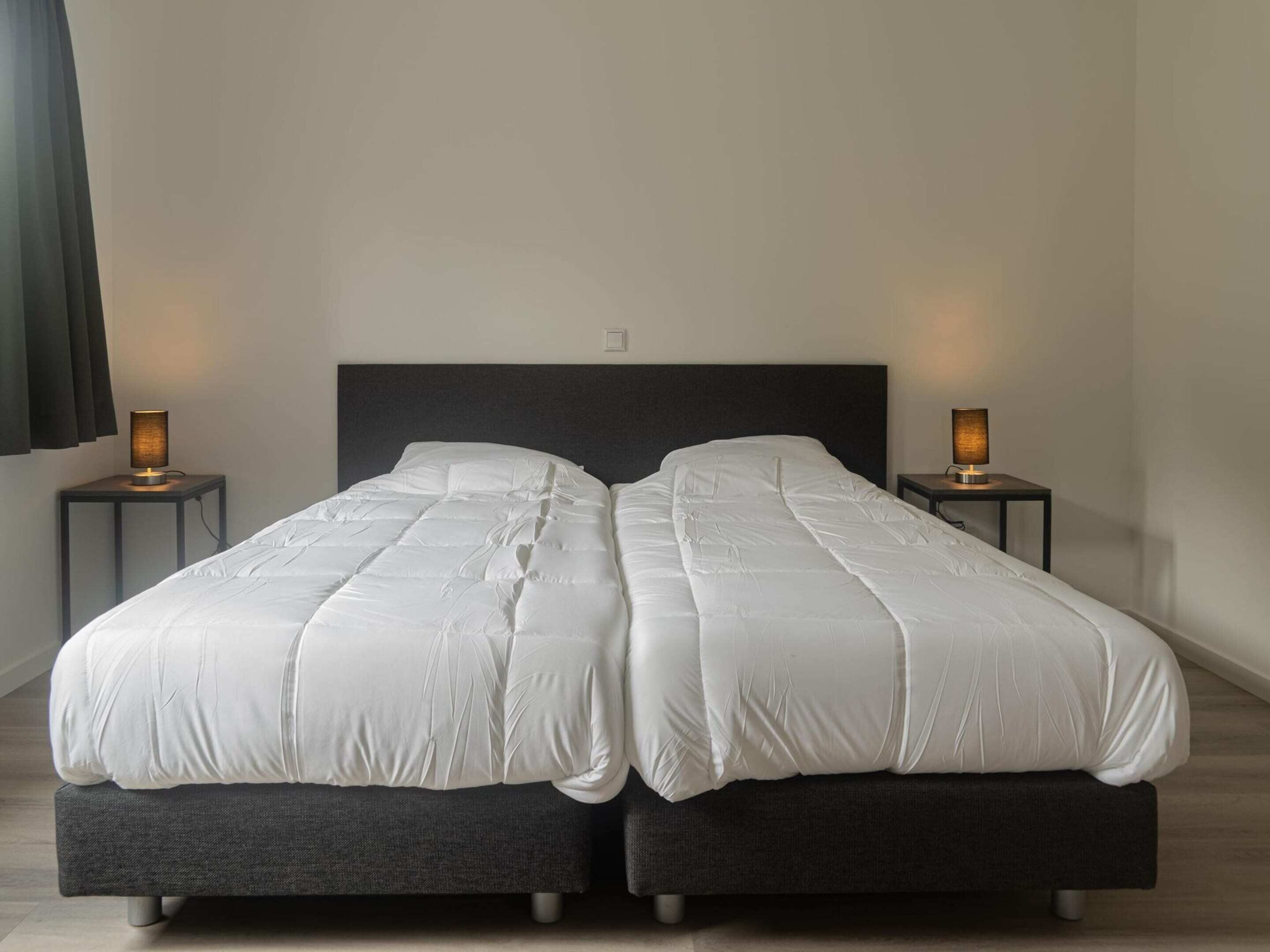 A double bed with a dark headboard, two bedside tables with lamps, and a plain wall.