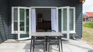 Een terras met een tafel en stoelen, een schuifdeur en een uitzicht op een keuken en een huis op de achtergrond.