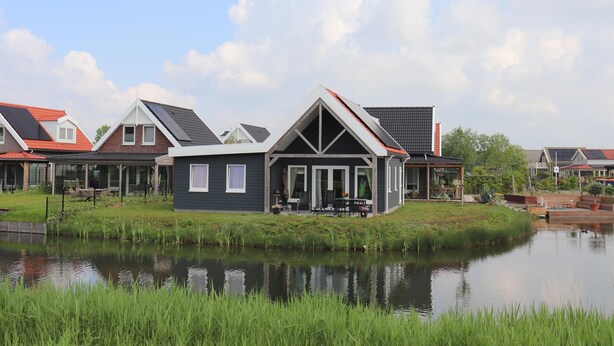 Een modern huis met een vijver ervoor, een overdekte patio en een rood dak.