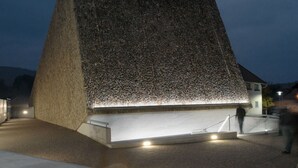 Ein großes, pyramidenförmiges Gebäude mit strukturierter Fassade und einem gut beleuchteten Eingang.
