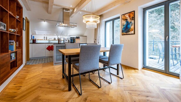 Eine moderne Küche mit Holzausstattung, ein Essbereich mit Tisch und Stühlen und ein großes Fenster mit Blick ins Freie.