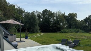 A hot tub with a patio area, outdoor furniture, and a view of a grassy field and trees. - Renovated house near beaches and golf (Bénodet)