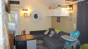 Un salon chaleureux avec un canapé gris, une chaise haute pour bébé, une petite table et un miroir décoratif.