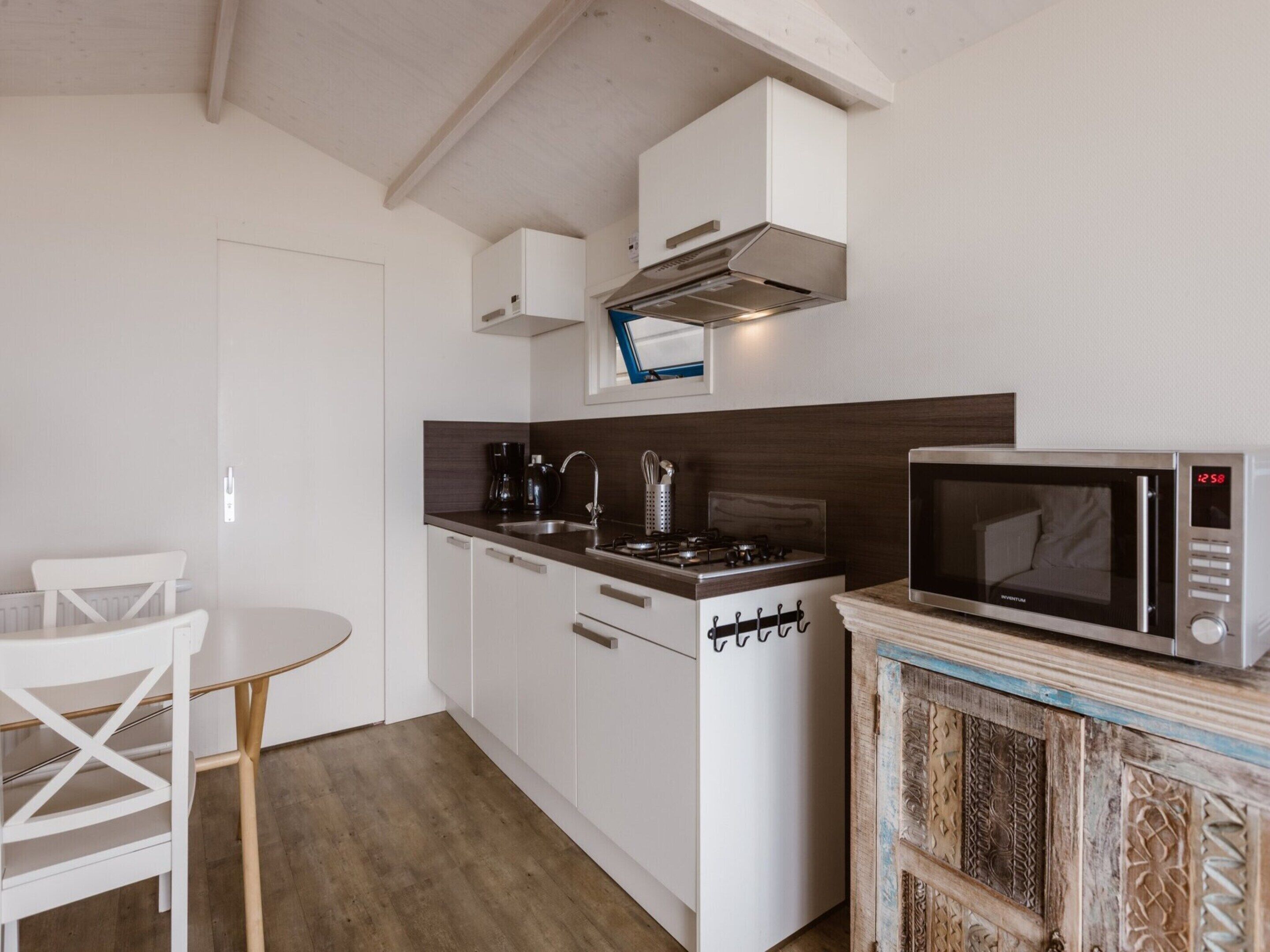 A compact kitchen with white cabinets, a stove, a microwave, and a small dining table.