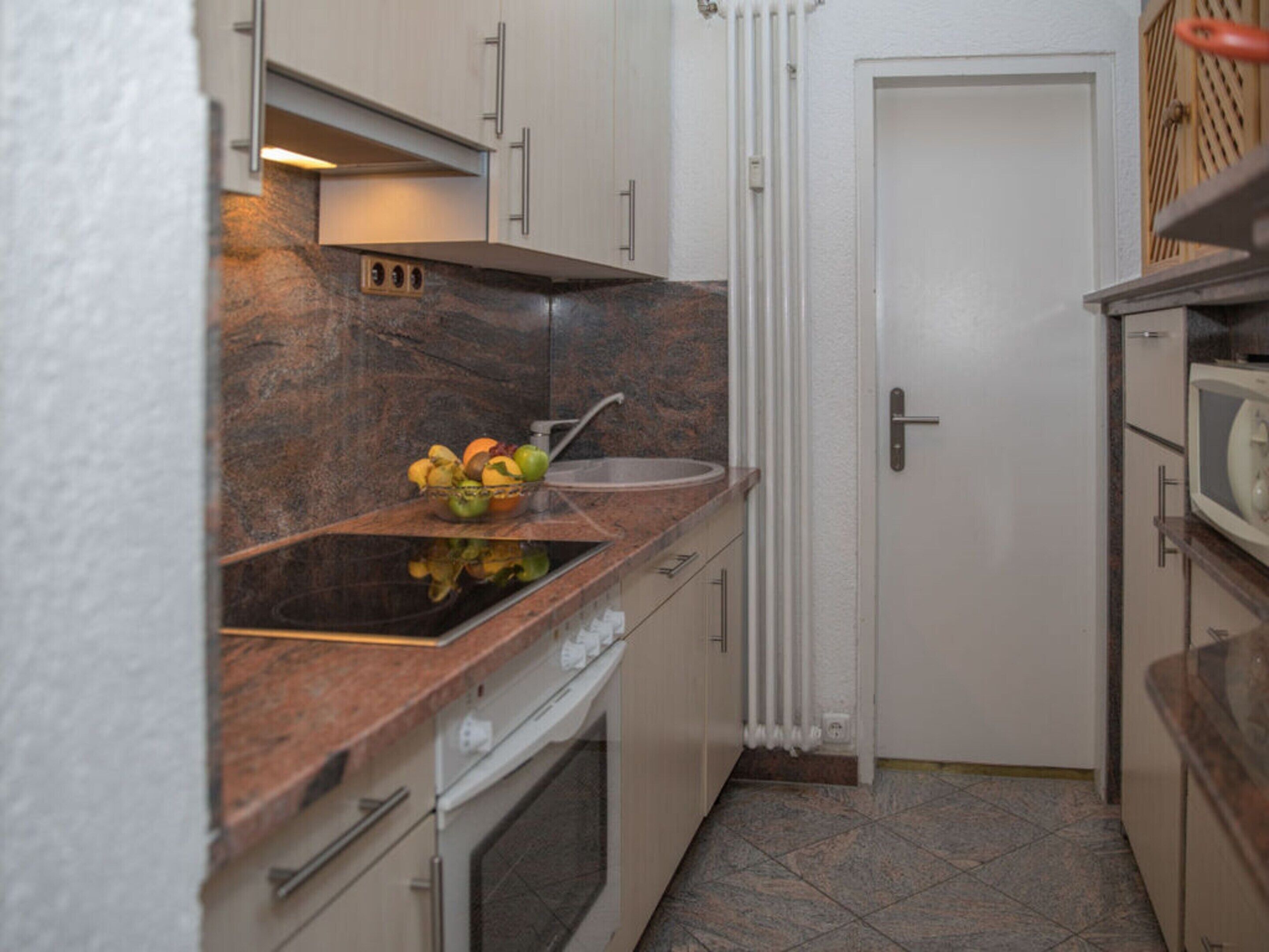 Eine kompakte Küche mit einer Granit Arbeitsplatte, einem eingebauten Backofen und einer weißen Tür.