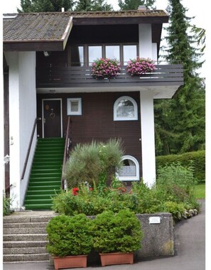A two-story house with a green staircase leading to the entrance, a small porch with flower boxes, and a well-maintained garden. - Lively Apartment in Bad Wiessee (Bad Wiessee)