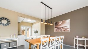 Eine moderne Küche mit Essbereich, mit einem Holztisch und weißen Stühlen, einer Uhr und Pendelleuchten.